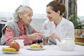 Elderly woman sharing tea with helpful looking smiling young woman in white